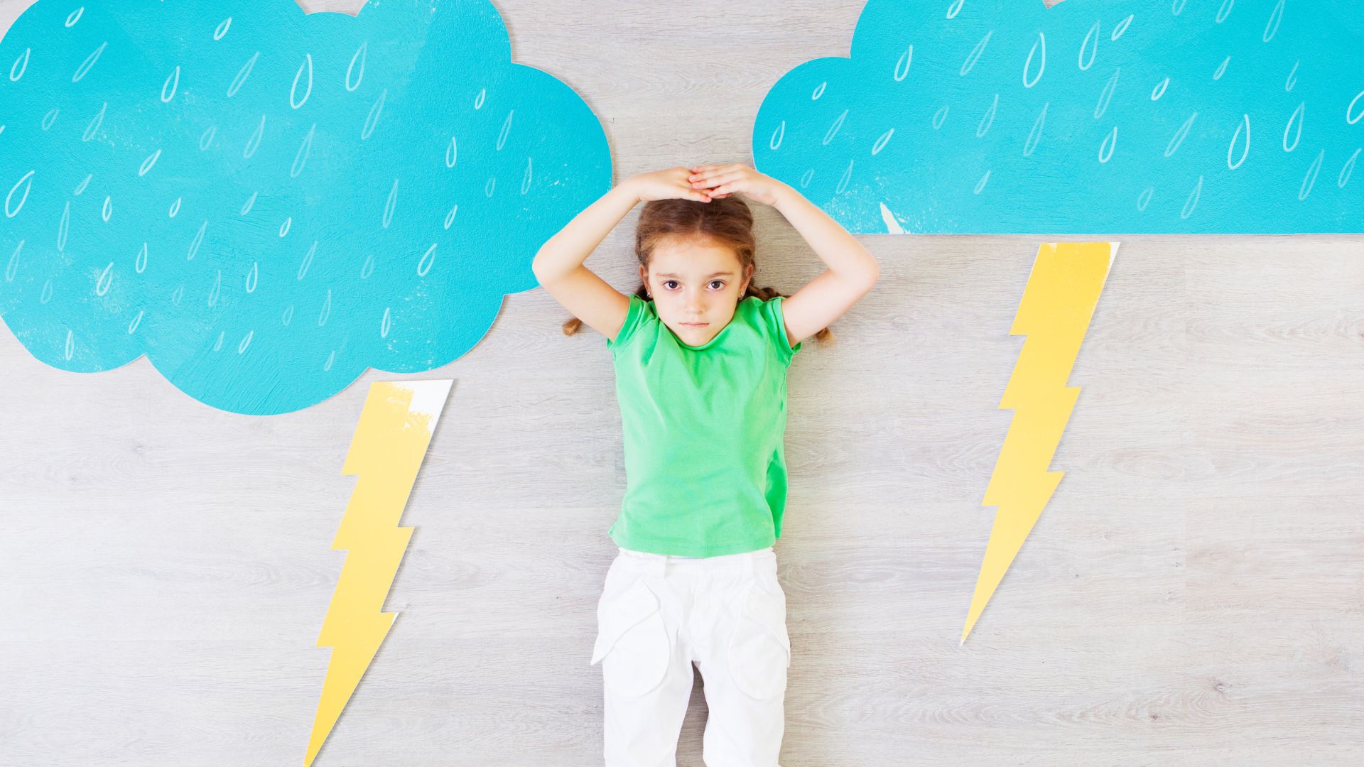 Jeune fille allongé au milieu de créations en papier représentant une météo pluvieuse, nuageuse et orageuse