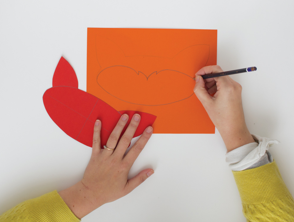 Personne en train de dessiner le contour d'un masque de carnaval renard dans du papier orange