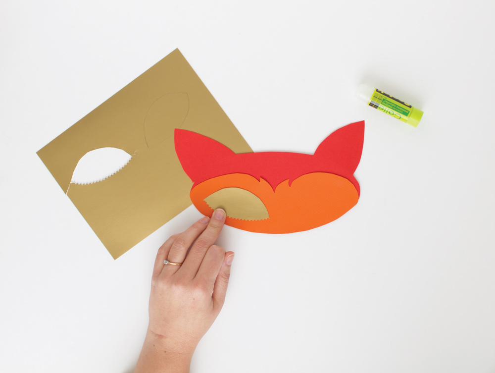 Personne en train de fabriquer un masque renard avec du papier doré et orange