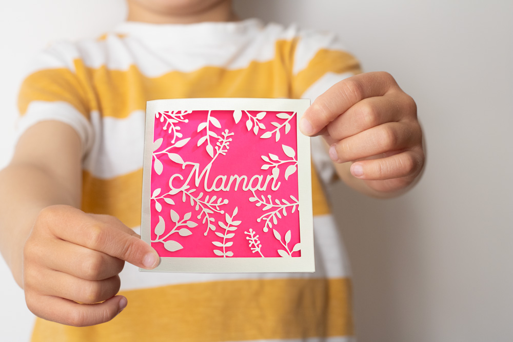 Enfant qui tient une carte de fêtes des mères découpée en papier avec un fond rose